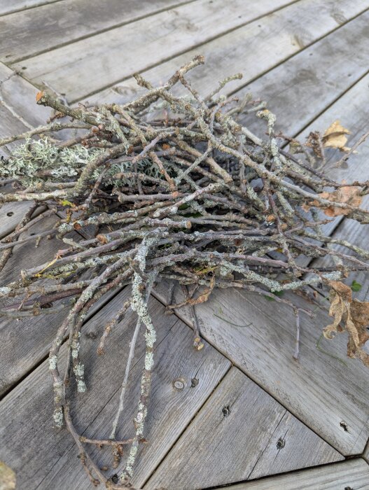 En hög av småekgrenar, delvis täckta med lav, ligger på ett trädäck.
