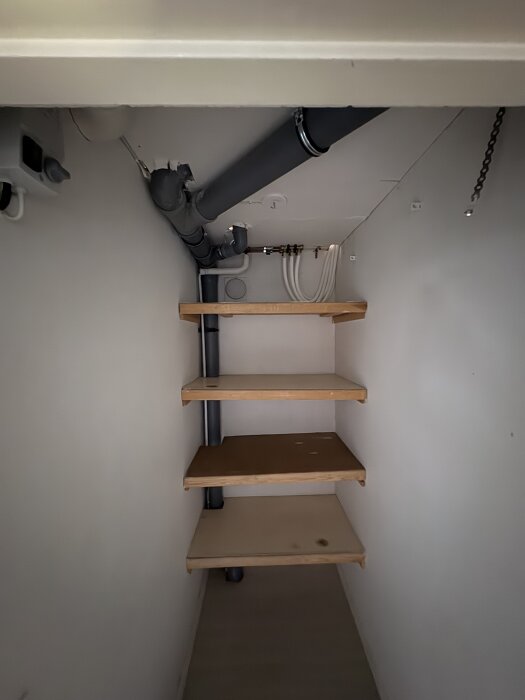 Hylla i hörn med flera rördragningar i taket, del av pågående badrumsrenovering.