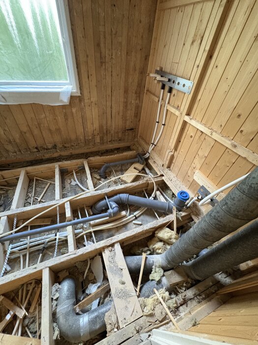 Öppen badrumsgolv med synliga rördragningar och panelvägg, under pågående renovering.