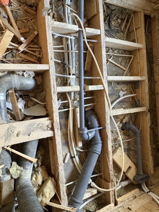 Badrumsrenovering med synliga rördragningar och träkonstruktioner i golvet, omgivna av byggmaterial.