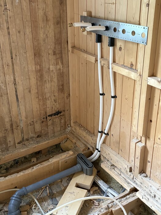 Rördragningar i ett halvfärdigt badrum med träram, avloppsrör och rörkopplingar synliga i ett pågående renoveringsprojekt.