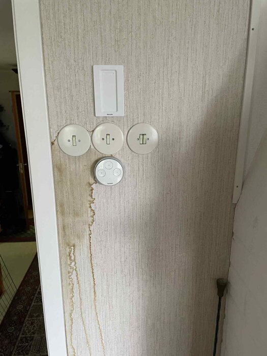 Vattenskadad tapetvägg med bruna fläckar vid ljusknapp och eluttag, orsakad troligen av läckage från skorstenen.