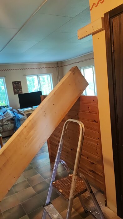 Limträbalk stöttad på ribbor i ett rum med stege framför, del av byggprojekt för att skapa en liten lägenhet.