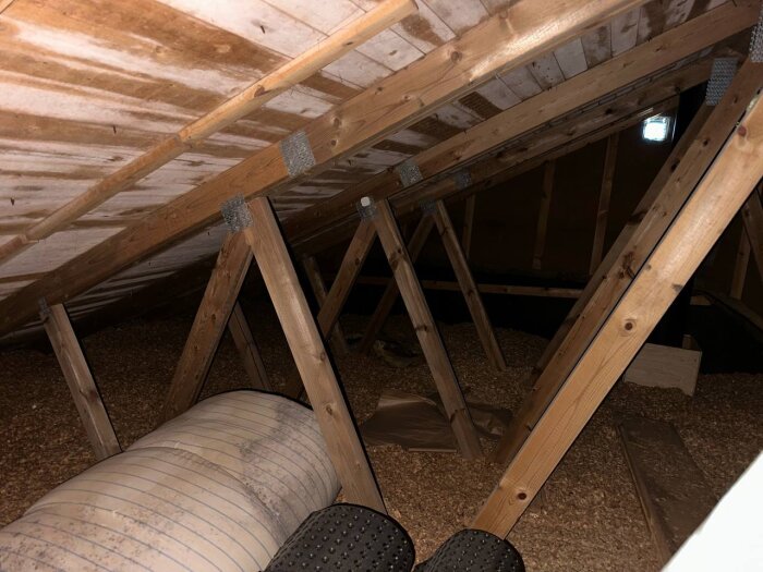 Vind med träbjälkar, isolering på golvet och tecken på fukt/mögel på insidan av taket. Gammal ventilation synlig i bild.