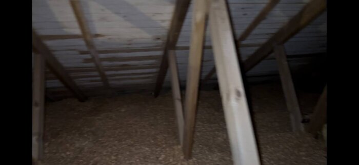 Vind med träbjälkar och träpanel samt isoleringsmaterial på golvet. Möjligt problem med mögel och ventilation.