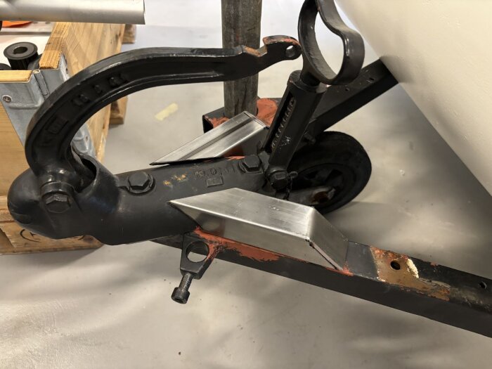 Koppling för släpvagn med metallkonstruktion och handtag, placerad på ett golv med träboxar i bakgrunden.