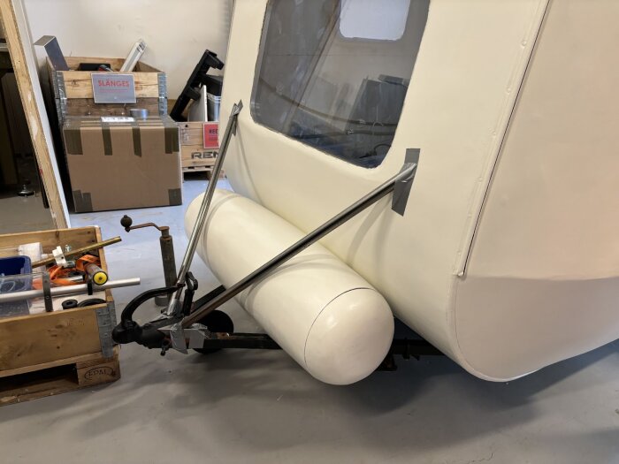 Vit husvagn med förstärkta stänger och tejp. Omkringliggande verktyg och kartonger i ett garage eller verkstad.