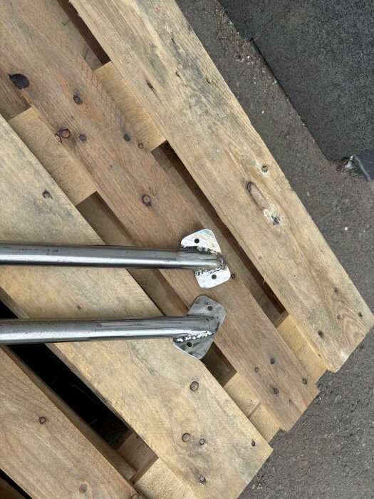 Två metallrör med fästen på en träpall, inför ett byggprojekt med spontanköpt tomt.