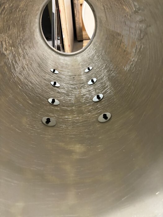 Inre vy av ett stort rör med bultar på insidan, trämaterial och andra byggdetaljer syns i bakgrunden.