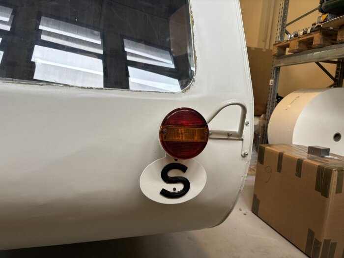 Bilden visar baksidan av en vit trailer med ett rött och orange bakljus och en oval skylt med bokstaven "S".