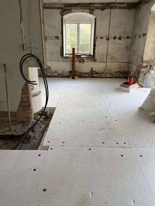 Renovering av gammalt stenhus med delvis borttagen kalkputs; golvet består av vita skivor, och ett fönster syns i bakgrunden.