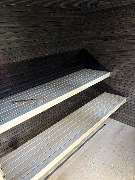 Bastu med nyinstallerade lavar av ljus trä; mörka träpaneler på väggar och tak. En tumstock vilar på lavarna.