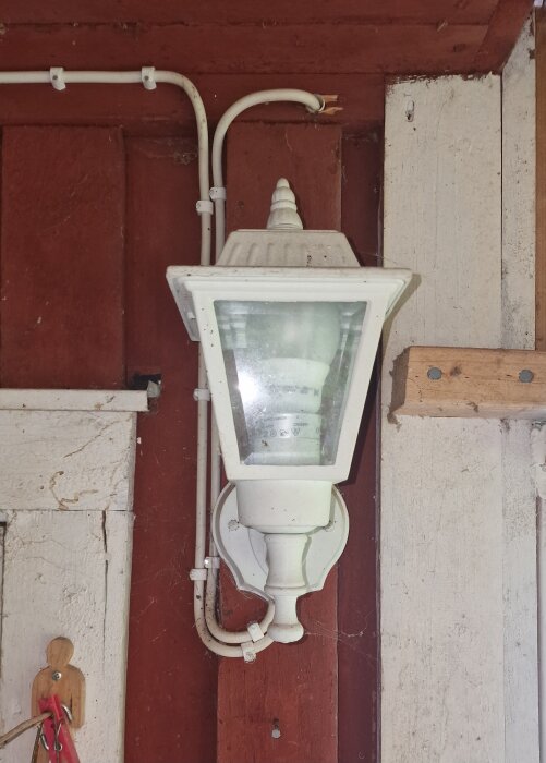 Utomhuslampa på röd vägg med vit kabeldragning längs väggen, del av renoveringsprojekt för att dölja kablar och installera mysbelysning.