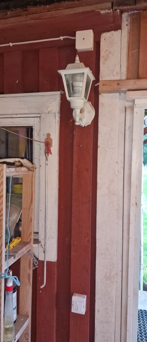 Bilden visar en vägg med en vit utomhuslampa och en dubbel strömbrytare; kablarna är dolda bakom en lockbräda.