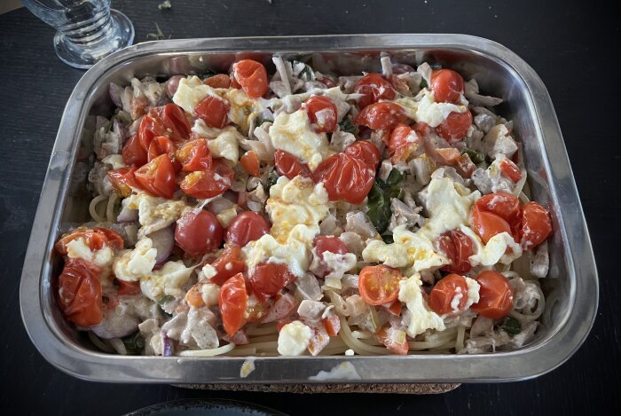 Pastagratäng med kyckling, tomater, mozzarella, lök, rädisor, paprika och padrones i en form på ett bord.