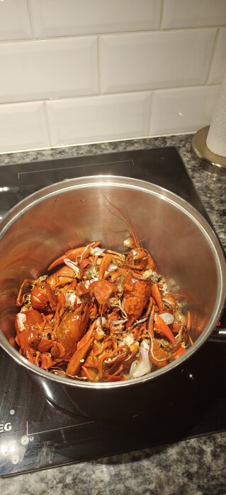 En gryta med kokta skaldjur, främst kräftor, står på en spis med vita kakelplattor i bakgrunden.