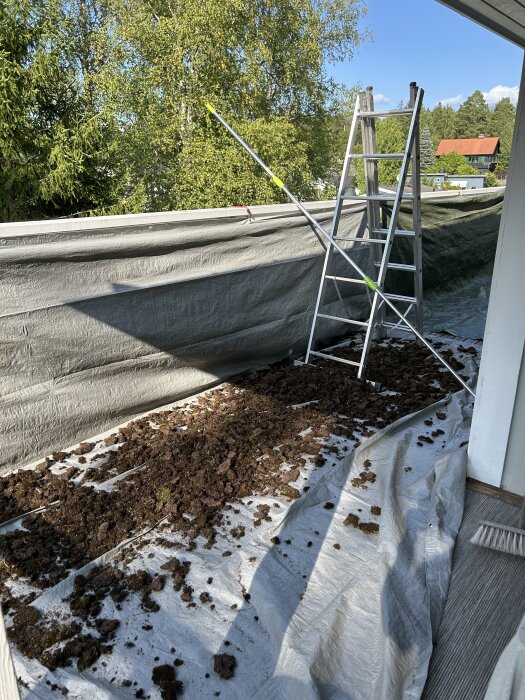 Stege och skrapa på tak med presenning täckt av bortskrapad mossa, omgivet av träd och ett rött hus i bakgrunden.