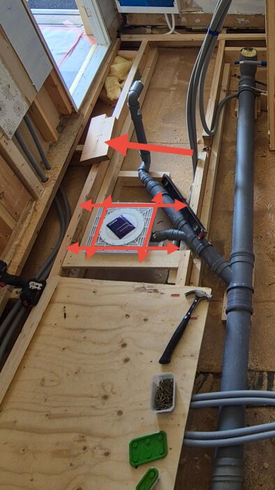 Renovering av golv med synliga träreglar, rör och verktyg. Röd pil markerar ett problemområde. Vibrationsdämpare och skruvar synliga på plywood.