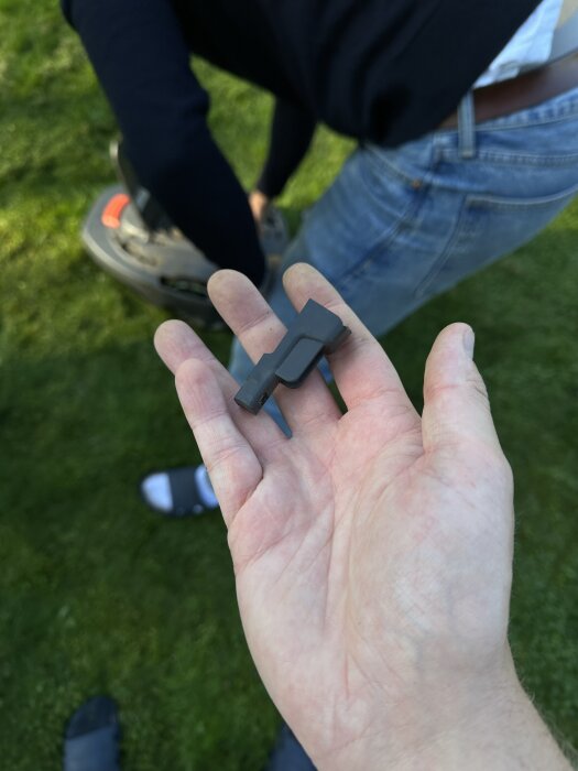 Hand håller en svart plastdel från en Gardena Sileno City 500 gräsklippare, bredvid en person som undersöker klipparen.