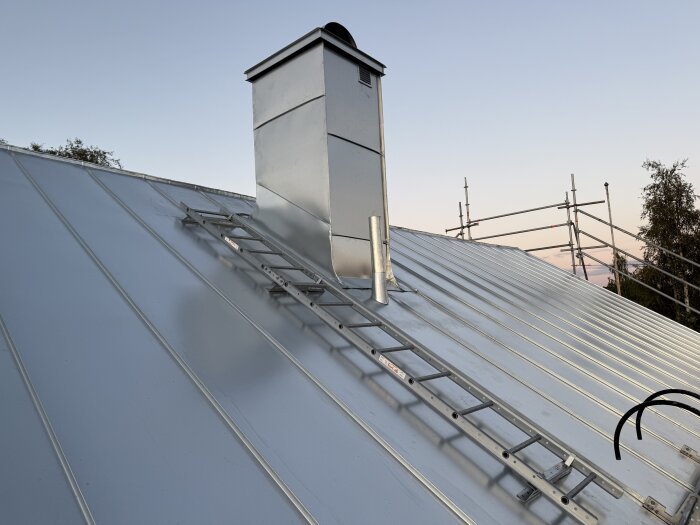 Nylagt tak med Plannja Zink Magnesium, reflekterar himlen. Synlig stege och skorsten, omgivande byggställningar.