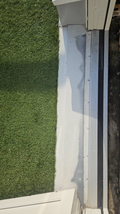 Altandörr med slitage på tröskeln, gräs vid sidan av dörren. Dörren verkar hänga och skava på tröskeln, skruvar syns i bild.