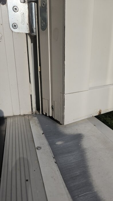 Närbild av en vit altandörr med gångjärn, där nederdelen av dörren skaver mot en metalltröskel. Dörren är aningen lutande och ej justerad.