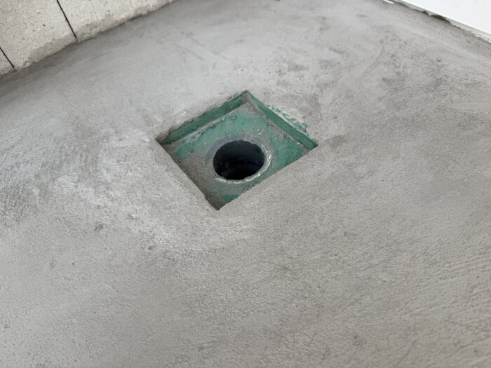 Cementgolv med grön golvbrunn under installation på en takterrass, visar öppning för avlopp utan tätskikt och olika materialytor.