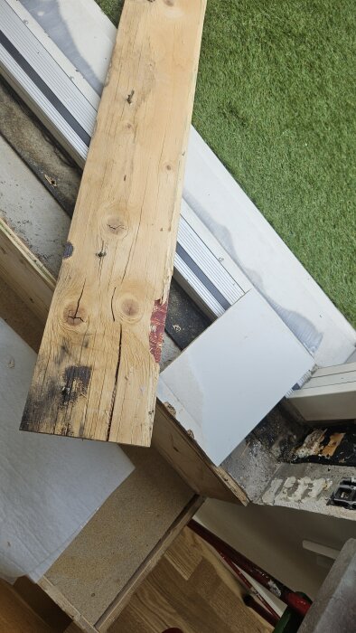 Svartmögel och fuktskadad träbröstning vid altandörr, delvis täckt av spånskiva och plankor, synliga fuktskador och försök till tätning.