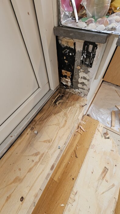 Skadat trä runt en altandörr med synligt svartmögel och flagnande färg, trägolvet är delvis avlägsnat, tecken på tidigare reparationer.