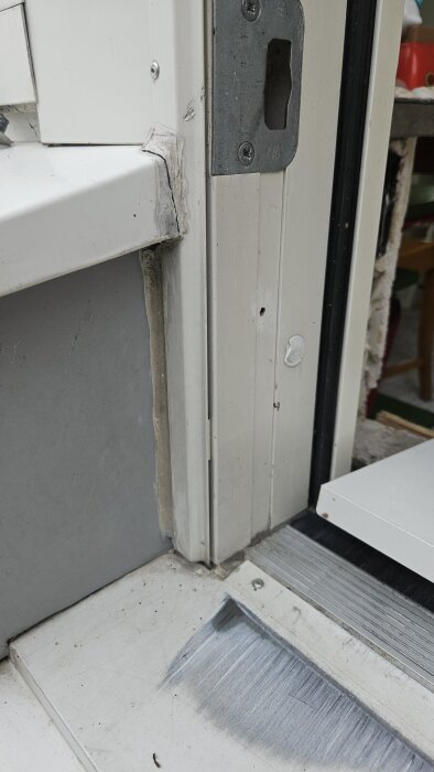 Närbild på en dörrkarm och tröskel med synliga tecken på vattenskada och tidigare lagning i hörnet.