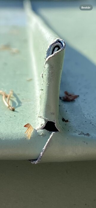 Skada på plåt. En närbild visar ett hål och skadad kant på en ljusgrön plåt, vilket kan kräva reparation inför slutbesiktning.