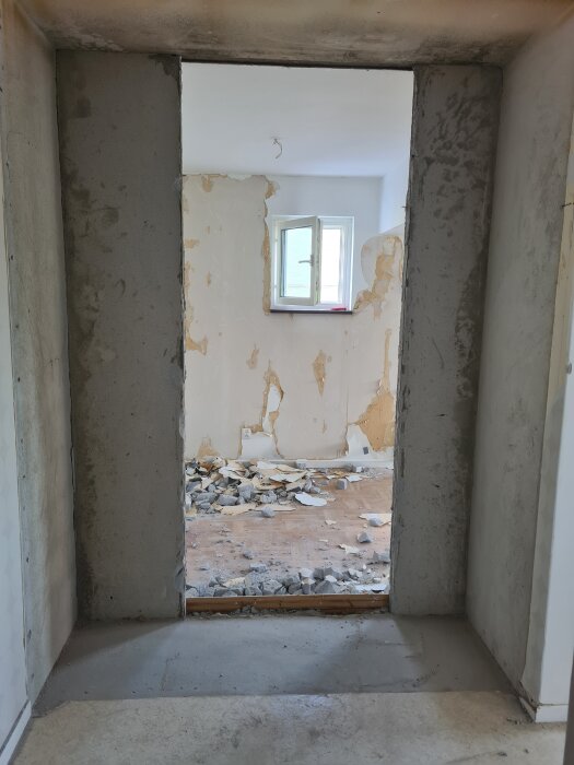 Genomgång utan vägg med murbruk och rivningsmaterial på golvet i ett rum med ett öppet fönster.