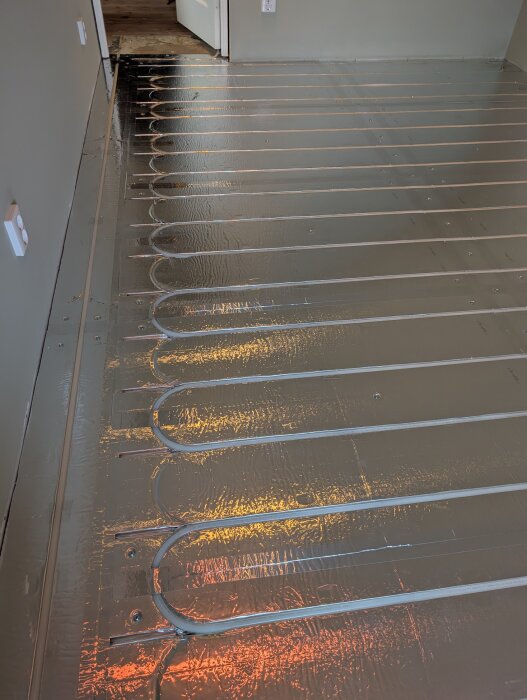Golvvärmeinstallation med LK Combiboard 18, visar golvvärmeslangar placerade i spår av reflekterande material i ett rum under renovering.