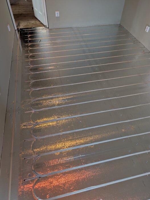 Golvvärmesystem med LK Combiboard 18-skivor och värmeslangar installerade i ett rum, reflekterande aluminiumyta syns.