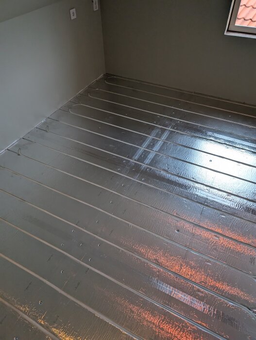 Golvyta med nylagda LK Combiboard 18-skivor i aluminium för golvvärmeinstallation, reflekterande och monterade i ett rum.