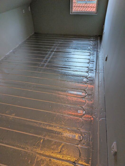 Nylagt golv med LK Combiboard 18 golvvärme-skivor i ett rum, med aluminiumtejpade skarvar synliga och reflektioner från ett fönster.