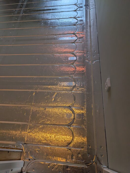 Golvvärmeinstallation med LK Combiboard 18 EPS-skivor och aluminiumtejp, visande fastskruvade skivor och anslutna rör i speglat ljus.