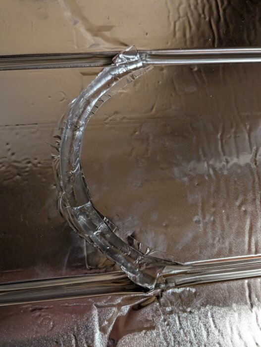 Närbild av golvvärmeslang i vändning, fäst med aluminiumtejp på en reflekterande yta.