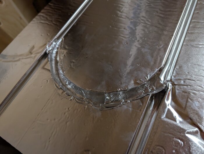 Golvvärmeskiva med reflekterande aluminiumtejp applicerad i en böj för optimal värmespridning.