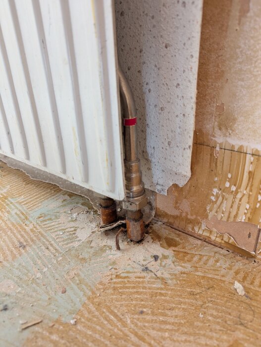 Elementkoppling med rör och ventiler, synliga vid golv och vägg, med tecken på läckage och byggdamm på golvet.
