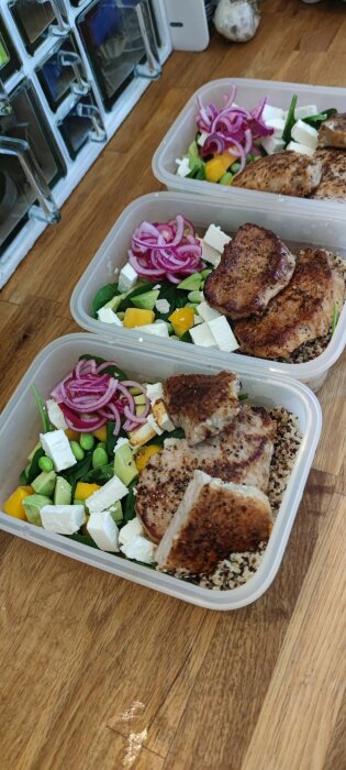 Tre matlådor med sallad, kotlett, rödlök och fetaost uppställda på en köksbänk i förberedelse för arbetsveckan.