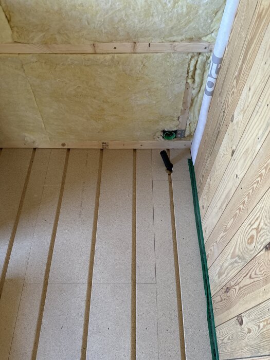 Spårade spånskivor på golvet i ett renoveringsprojekt med synliga korsande reglar och isolering i väggarna.