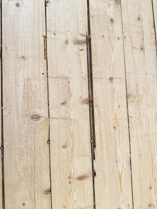 Gammalt furugolv med synliga kvistar och sprickor, potentiellt slitet.