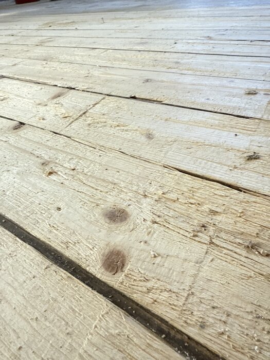 Gammalt furugolv med synliga skavanker och kvistar, nyligen exponerat efter att ha avlägsnat ekparkett.