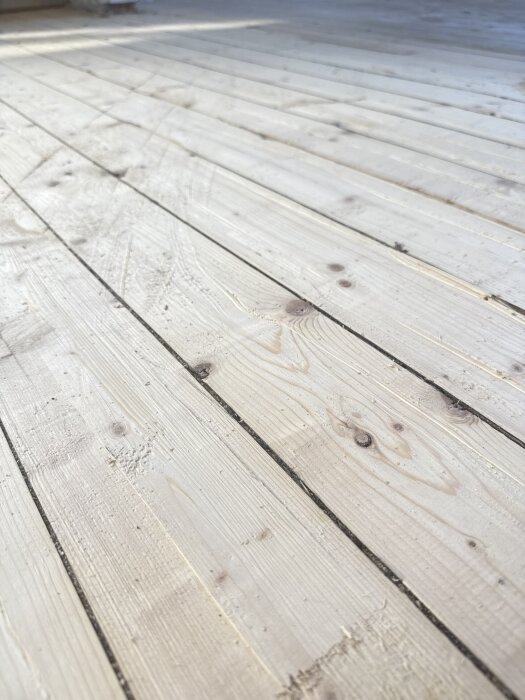 Gammalt furugolv i närbild, delvis slitet och med synliga repor, undersöks för potentiell renovering.