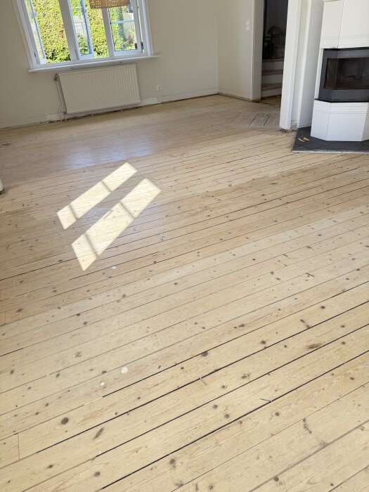 Ett 98 år gammalt furugolv i ett rum med öppen spis och stort fönster, visar slitage och skador.