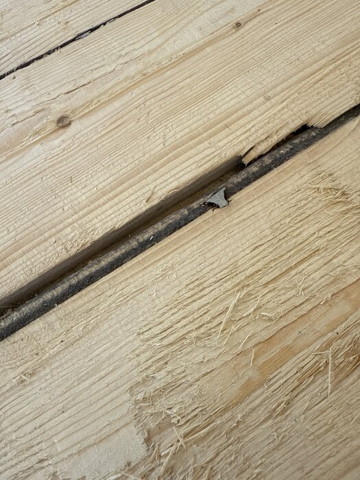 Närbild av 98-årigt furugolv med slitna och ojämna plankor, synliga springor och märken.