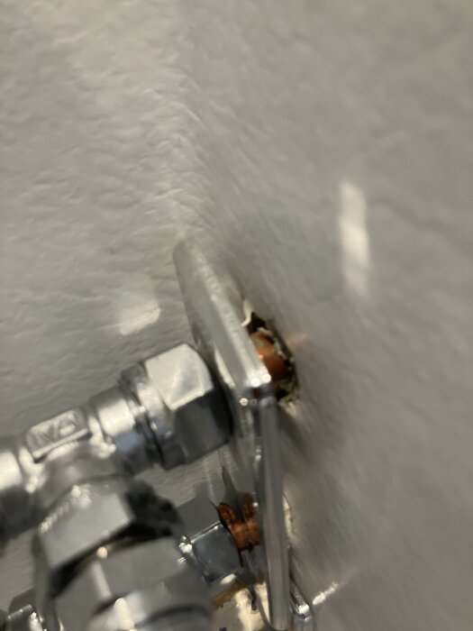 Rörgenomföring med metallrör och kopplingar genom våtrumsvägg/plastmatta. Möjligen otillräckligt tätad runt genomföringen.