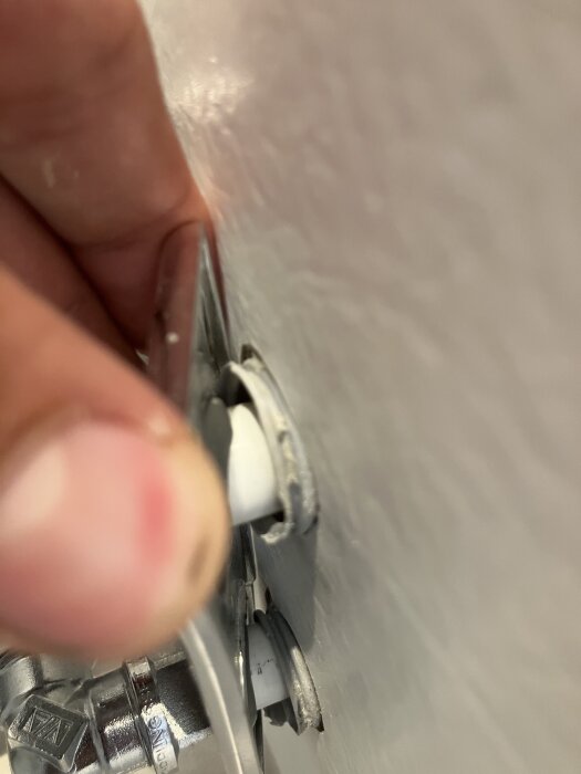 Närbild av en rörgenomföring i ett badrum med synliga rör och plastmatta från Tarkett, inspekterad av en hand.