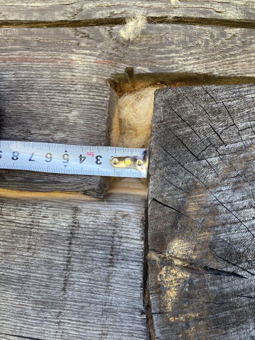 Mätband visar 4 cm glipa i nybyggt timmerhus vid laxknut, med synligt isoleringsmaterial.